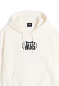 Sweat à capuche de couleur crème avec un logo Vans noir en forme ovale. Le matériau semble doux, avec une poche kangourou et une capuche à cordon.
