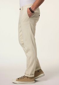 Beige chino's met een rechte pasvorm, voorzien van zijzakken, een knoopsluiting en opgerolde zoom, gecombineerd met bruin hoge sneakers.