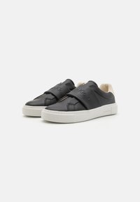 Sorte skinnslippers med en kremfarget fôr, med synlig Calvin Klein-logo og en hvit gummisåle.