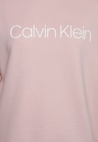 Lichtroze sweatshirt met een zachte textuur, voorzien van het "Calvin Klein" logo in vette witte letters gecentreerd op de borst.
