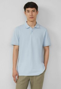 Hellblaues Poloshirt aus weichem Stoff mit einer Knopfleiste mit zwei Knöpfen und kurzen Ärmeln. Dezentes Logo-Detail auf der Brust.