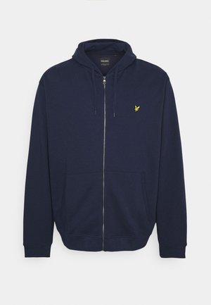 Sweat à zip bleu marine fabriqué en tissu doux, avec une poche kangourou et un petit emblème jaune sur le côté gauche de la poitrine.