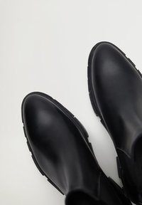 Zwarte leren enkellaarsjes met een soepele afwerking, rubberen zool en minimalistisch design. Licht afgeronde neus en elastische zijpanelen.
