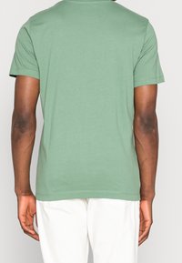 Grön bomullströja med korta ärmar, rund halsringning och en mjuk textur. Bakifrån visas en enkel, odekorerad design.