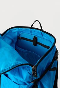 Εσωτερικό μπλε σακιδίου με φερμουάρ, με μια δομημένη τσέπη και μαύρα εξαρτήματα. Διαθέτει λεία, γυαλιστερή υφή και ανθεκτικό ράψιμο.