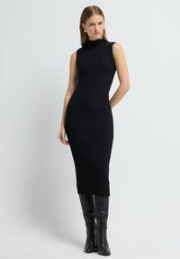 Czarna prążkowana dzianinowa sukienka bez rękawów z wysokim dekoltem, dopasowana sylwetka i długość midi, w połączeniu z gładkimi czarnymi kozakami do kolan.