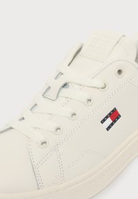 Λευκό αθλητικό παπούτσι Tommy Jeans με λευκά κορδόνια, ραμμένες λεπτομέρειες και μικρό κόκκινο, λευκό και μπλε λογότυπο στο πλάι.
