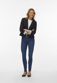 Schwarzes Blazer mit einem cropped Design, grauem gestreiften Manschettendetail, kombiniert mit einem weißen T-Shirt und dunkelblauen engen Jeans sowie schwarzen High Heels.