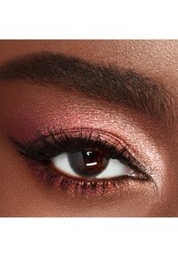 Primo piano di un occhio con un ombretto luminoso e caldo nelle tonalità di rosa e bronzo, ciglia nere e sopracciglia ben definite.