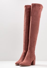 Różowe, zamszowe kozaki do kolan o smukłym nosku i grubej podeszwie, z gładką strukturą i bezszwowym wzornictwem.