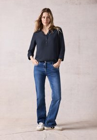 Zwarte blouse met knoopsluiting en een kraag, gecombineerd met blauwe flared jeans en witte sneakers. Glad materiaal en een casual pasvorm.