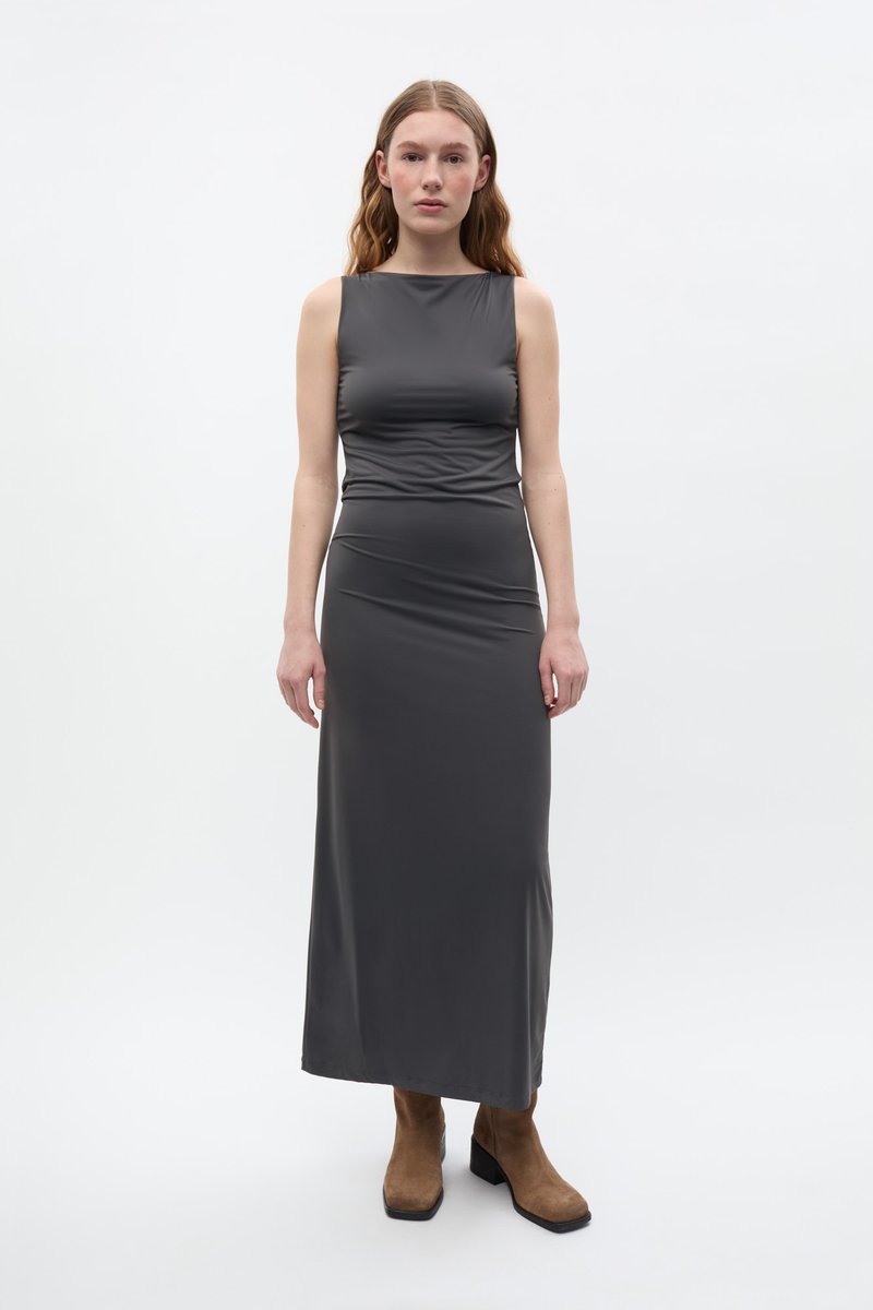 Largo vestido gris ajustado con un diseño sin mangas y detalles fruncidos en la cintura. Combinado con botas de tacón grueso marrones.