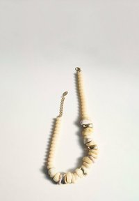 Collier en perles avec des pierres beige crémeux et des accents métalliques. Des éléments alternant lisses et texturés créent un intérêt visuel.
