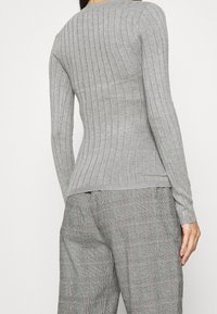 Maglietta grigia a maniche lunghe con un design aderente, scollo rotondo e texture sottile, abbinata a pantaloni a quadretti grigi con motivo a check.