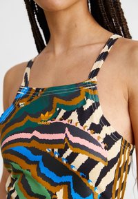 Multicolored tank top featuring a wavy pattern in green, blue, black, and pink; made of smooth fabric with adjustable straps and an Adidas logo.