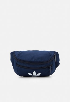 Banane en tissu bleu marine avec deux compartiments zippés et un logo trèfle blanc sur la poche avant.