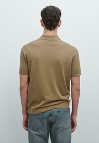 Koszulka polo z krótkim rękawem w jasnobrązowym kolorze, wykonana z miękkiego materiału. Posiada kołnierzyk oraz prążkowany dół, zestawiona z jasnymi dżinsami.