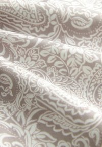 Tessuto morbido con un delicato motivo floreale paisley beige e bianco, che mostra pieghe e texture alla luce naturale.
