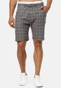 Shorts à carreaux gris avec une taille à cordon, des poches latérales et un tissu léger. Le motif présente de fines lignes blanches contrastant avec le fond gris.