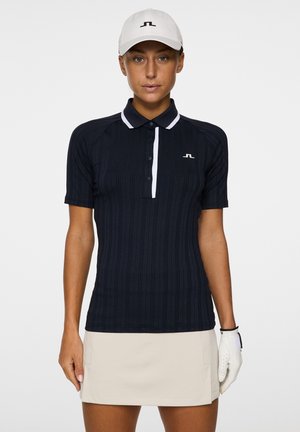 Marineblaues Golfpoloshirt mit kurzen Ärmeln und vertikal geripptem Design, weißer Kragen und Knopfleiste, besticktes Logo, kombiniert mit einem beigen Rock und einem weißen Handschuh.