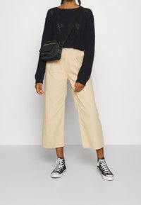 Pull tricot navy à maille ouverte, pantalons larges crème, et baskets montantes noires. Petit sac bandoulière noir.