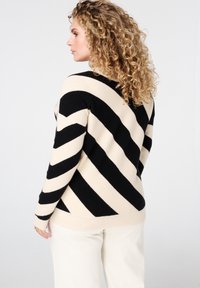 Gestreepte trui in zwart en beige, met een chevronpatroon, geribbelde manchetten en een losse pasvorm. Gemaakt van een zachte gebreide stof.