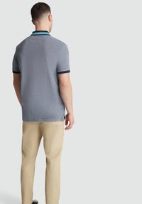 Polo gris avec un tissu texturé, accents de col bleu marine et manches courtes. Assorti à un pantalon beige clair, vu de l'arrière.