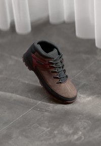 Brown and black leather hiking shoe with a padded collar, rubber sole, and grey laces. Features a maroon accent on the side.