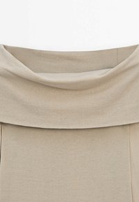 Beżowa bluzka na ramiączka, wykonana z miękkiego, elastycznego materiału, z luźnym, drapowanym dekoltem i dopasowanym fasonem na korpusie.