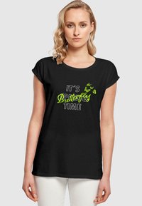 Svart bomull T-skjorte med korte ermer har et trykt design i hvit og neon grønn tekst som sier "DET ER VÅR, SOMMERTID FOR SOMMERFUGLER," med sommerfuglgrafikk.