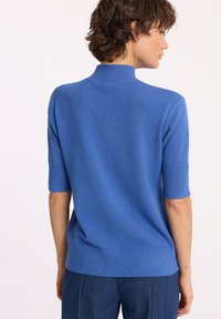 Niebieski sweter z krótkim rękawem, z wysokim kołnierzem, prążkowymi mankietami i dołem, wykonany z miękkiego, teksturowanego materiału dzianinowego.