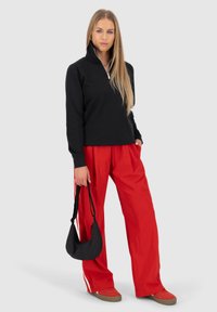 Felpa nera con zip, pantaloni a gamba larga rossi, borsa a tracolla nera. Sneakers con suola marrone. Tessuto liscio con una trama sottile.