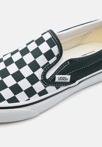 Vans slip-on tenisky s kanvasovým zvrškom v zelenej a bielej kostkovanej vzore, čiernym lemovaním, polstrovaným golierom a bielou gumovou podrážkou.