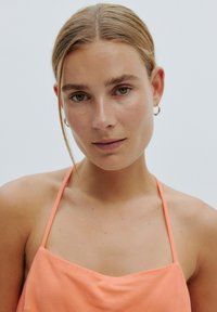 Satin-Camisole in zartem Pfirsich, mit dünnen Trägern und lockerem Schnitt. Glatte Textur mit leichtem Glanz und minimalistischem Design.
