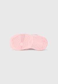 Vaaleanpunainen kuminen lenkkaripohja, jossa on teksturoitu kuvio, jossa on ympyrä- ja viivakouruja. Nike-logo näkyvissä sivulla.
