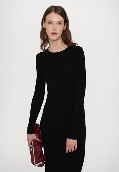 Vestido negro de manga larga con canalé y cuello redondo, combinado con un bolso tipo clutch de color rojo oscuro con detalles metálicos.