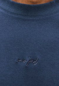 Tumši zila sporta džempera ar apaļu kaklu un mīkstu tekstūru. Priekšpusē ar sakrītīgu diegu izšūts teksts "mo'd".