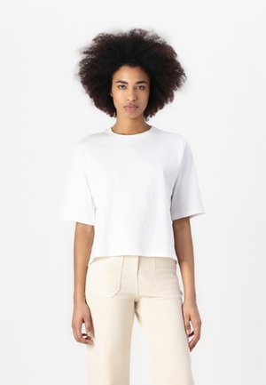 Weißes, kurzes T-Shirt mit kurzen Ärmeln und rundem Ausschnitt, aus weicher Baumwolle, kombiniert mit hellbeigen, hoch taillierten Hosen. Einfaches Design.