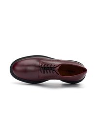 Scarpa oxford in pelle rosso scuro con lacci neri e suola nera spessa, vista dall'alto su sfondo bianco.