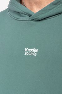 Felpa verde con una texture liscia, caratterizzata da un logo frontale che riporta la scritta "Kaotiko society" in bianco. Includere cappuccio e design in morbido tessuto.
