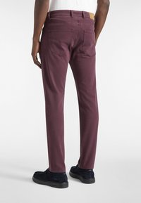 Bordo pamučne hlače s četiri džepa, slim fit dizajn i kožna oznaka na pojasu. Nosite ih s mornarskim slip-on cipelama.