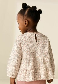 Blusa con estampado floral en blanco roto con acentos en rosa y amarillo, que presenta una espalda con abertura en forma de ojo de cerradura, mangas largas y un dobladillo con volantes.