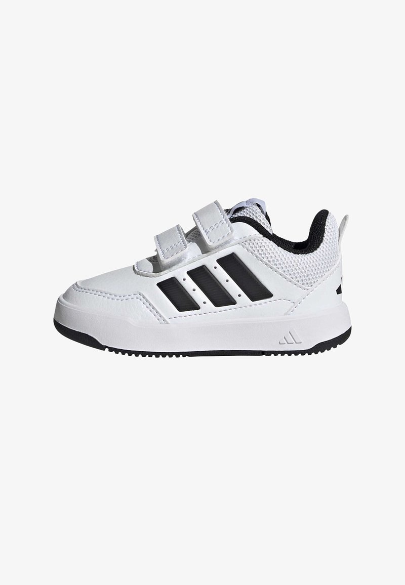 Bijela sportska cipela s crnim detaljima, mrežastim gornjim dijelom, dva remena s pričvršćivanjem na čičak i gumeni potplat. Ima tri crne pruge sa strane.