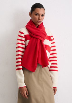 Red wool scarf draped around neck, paired with a cream sweater featuring bold red stripes, layered over a beige skirt. Smooth texture.