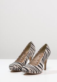 Black and beige zebra-striped high-heeled pumps with a rounded toe, smooth texture, and a wooden heel.