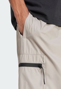 Beige lätta shorts med en sidficka och svart dragkedja. Tyget har en slät, något texturerad yta.