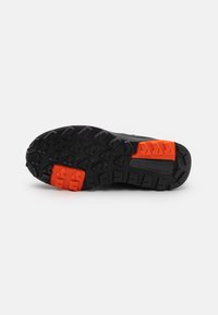 Svarte gummisåler med dype mønstre for godt grep, med oransje detaljer ved hælen og midtsålen. Holdbare og designet for godt feste.