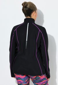 Sort atletikjakke med lilla accenter og høj krave. Har en reflekterende lodret stribe ned ad ryggen og et tekstureret stof.