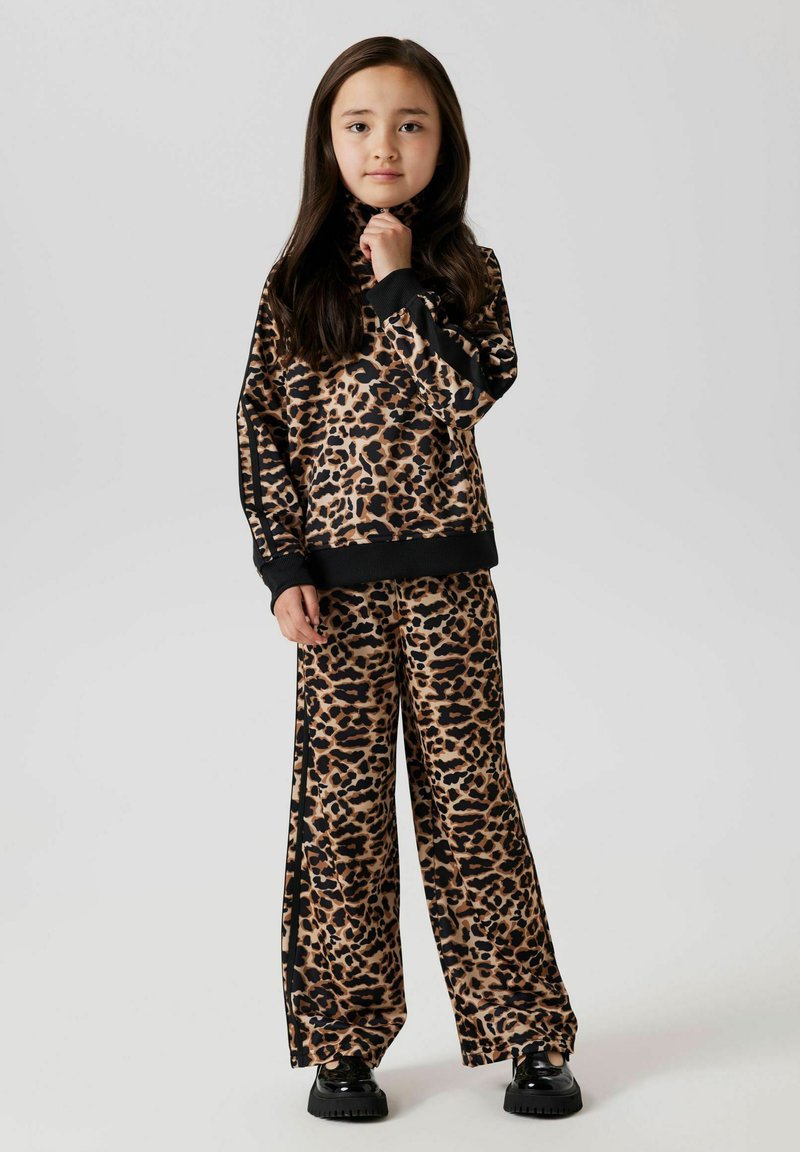 Ensemble deux pièces à imprimé léopard en tissu doux. Comprend un haut à col montant avec des manches longues et un pantalon large. Accents noirs le long des bords.