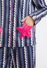 Gestreepte pyjama's in marineblauw en lichtblauw met roze golvende patronen. Voorzien van roze stervormige zakaccenten en bijpassende knopen.